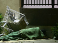 A homeless person sleeps on a downtown sidewalk