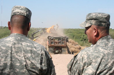 
                    Two soldiers on border patrol supervise the removal of a pile of dirt, so that Border Control can see the banks of the Rio Grande.
                                            (Michael May)
                                        
