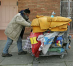 A poor man pushes his shopping cart through a ... 