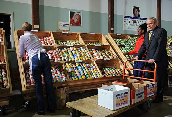 
                President Bush pushes a cart as volunteers load groceries during his visit to the Central Virginia Food Bank today in Richmond, Va.
                                    (Mandel Ngan/AFP/Getty Images))
                                