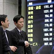Businessmen walk past share prices board in Tokyo 