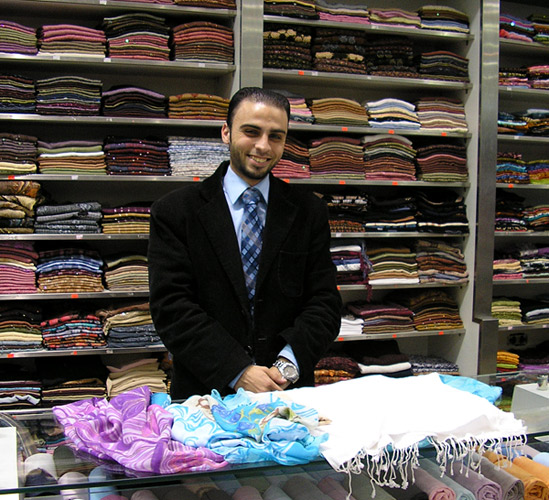 
                Lowei shows some of the hijab, or headscarves, he sells at Sajeda, a store in Amman's Mecca Mall. (And yes, it is a shopping mecca!) On the shelves behind him are dozens more.
                                    (Alisa Roth)
                                