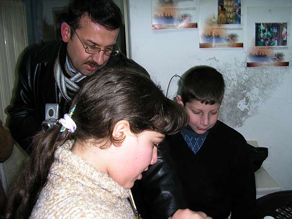 
                Maher, Taghreed and Abdulelah in the "dining room." On the wall behind them, photos of the kids are mounted on makeshift frames made from the pages of an old giveaway calendar.
                                    (Alisa Roth)
                                