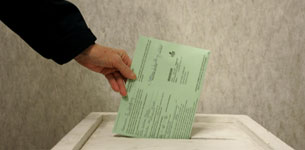 A woman drops her ballot in a voter box .
