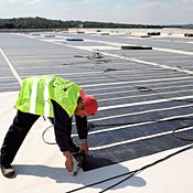 Worker staples photovoltaic solar panels on roof 