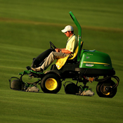 A grounds crewman on a John Deere mower 