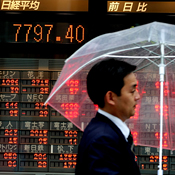 Man in umbrella walks past stock board in Toyko 