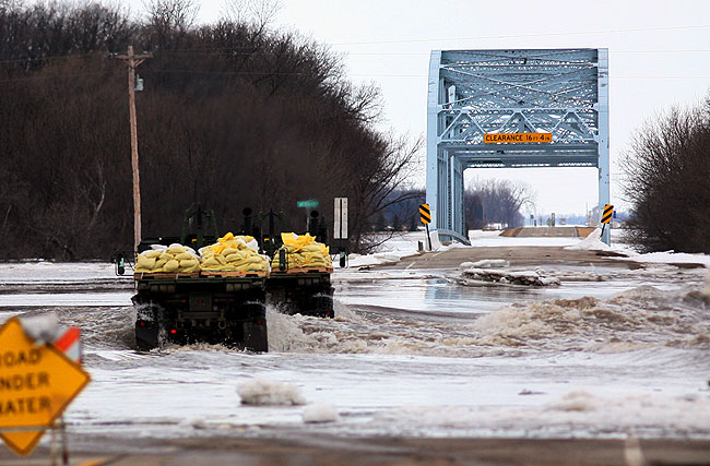 Military vehicles navigated over a flooded road as they delivered sandbags to a nearby farmstead in Hendrum, Minnesota, March 30, 2009. Officials in Hendrum and other Red River towns downstream from Fargo-Moorhead are concerned that a proposed flood diversion project will increase flooding in their areas.