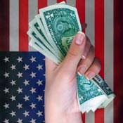 Hand holding dollars with U.S. flag in background 