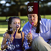 A Shriner helps a young girl blow bubbles 