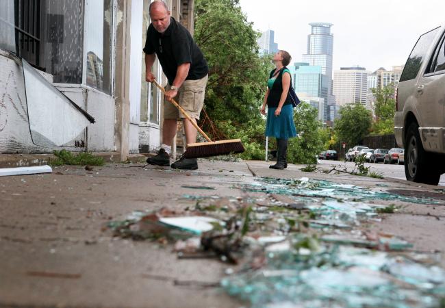Mark Herman sweeps broken glass after a friend's storefront window was broken as Jaim'ee Bolte examines the damage Wednesday, August 19, 2009.
