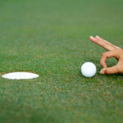 A finger poised to flick golf ball into hole 