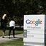Pedestrians walk by a Google sign