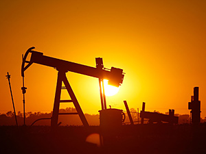 The sun sets behind an oil well