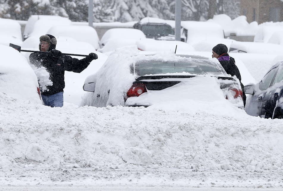 Workers remove snow at an auto dealership