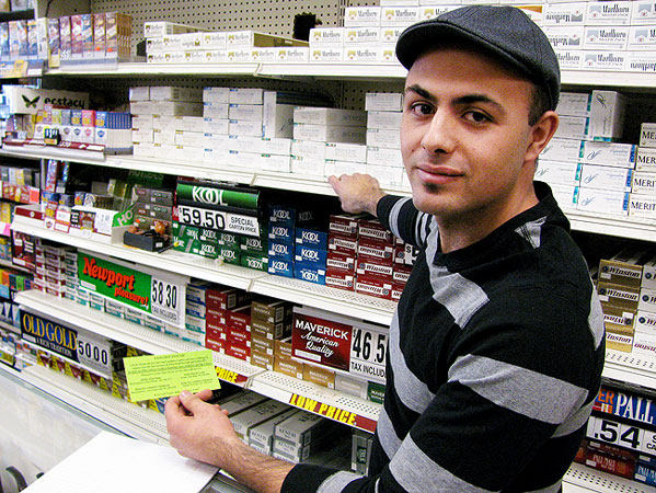 At Maplewood Tobacco, store manager Anan Barbarawi is not a fan of proposals to increase the tobacco tax, making cigarettes more expensive. He's holding a bright neon green card that urges customers to speak out against proposals to increase cigarette taxes in Minnesota.
