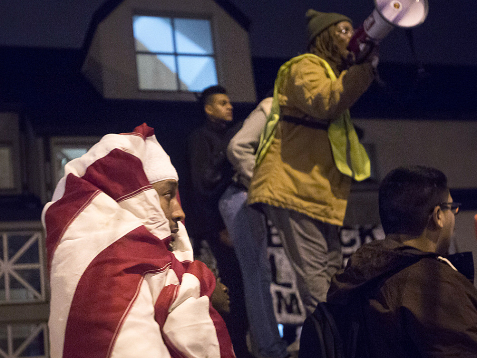 A protester wearing an American flag listened as a speaker from Black Lives Matter rallied other demonstrators in front of the 4th Precinct police station.